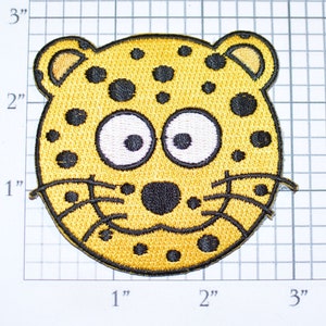 May include: A yellow and black embroidered iron-on patch of a cartoon leopard face with white eyes and a black nose.