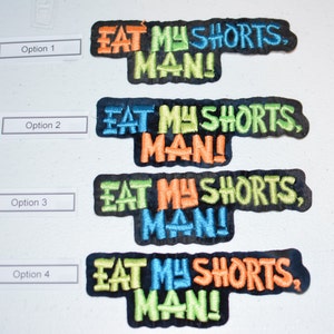 May include: Four embroidered iron-on patches with the text "EAT MY SHORTS, MAN!" in different color combinations. The patches are on a white background.