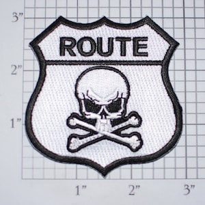 May include: White and black embroidered patch with a skull and crossbones design. The patch is shaped like a highway sign and says "ROUTE" at the top.