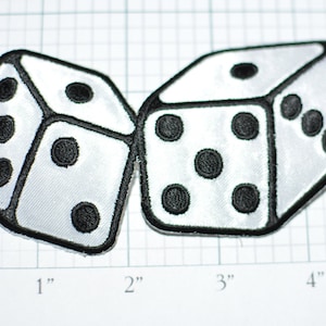 May include: Two white dice with black dots, each die has a different number of dots, the dice are sewn onto a white fabric background.