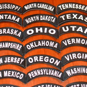 Puede incluir: Una colecci&oacute;n de parches bordados en blanco y negro, cada uno con el nombre de un estado de EE. UU. en un dise&ntilde;o curvo y arqueado. Los parches est&aacute;n dispuestos sobre una superficie de madera. Los estados incluyen Mississippi, Montana, Carolina del Norte, Dakota del Norte, Nebraska, Ohio, Nuevo Hampshire, Oklahoma, Nueva Jersey, Nuevo M&eacute;xico, Oreg&oacute;n, Pensilvania y Washington.
