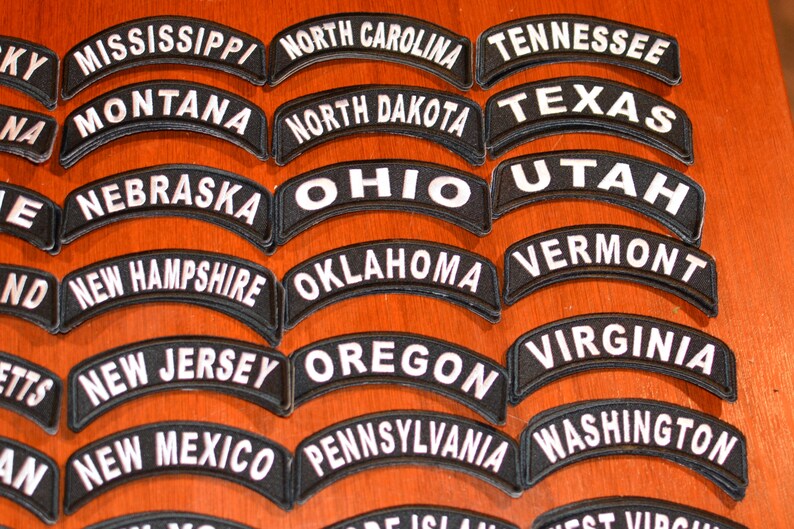 Puede incluir: Una colecci&oacute;n de parches bordados en blanco y negro, cada uno con el nombre de un estado de EE. UU. en un dise&ntilde;o curvo y arqueado. Los parches est&aacute;n dispuestos sobre una superficie de madera. Los estados incluyen Mississippi, Montana, Carolina del Norte, Dakota del Norte, Nebraska, Ohio, Nuevo Hampshire, Oklahoma, Nueva Jersey, Nuevo M&eacute;xico, Oreg&oacute;n, Pensilvania y Washington.