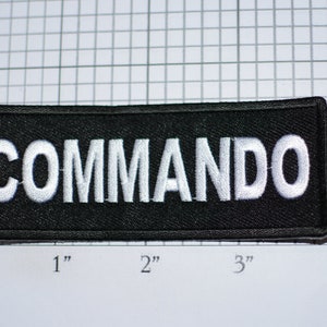 May include: Black patch with white embroidered text that reads "COMMANDO".