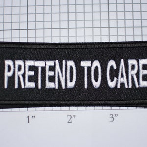 May include: Black embroidered patch with white text that reads "I PRETEND TO CARE".