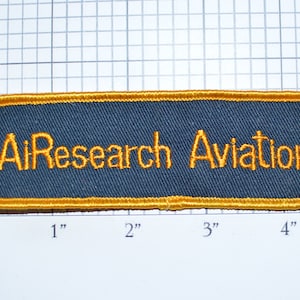 May include: A dark blue rectangular patch with a gold border and the text "AiResearch Aviation" embroidered in gold.