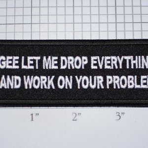 May include: Black rectangular patch with white embroidered text: "GEE LET ME DROP EVERYTHING AND WORK ON YOUR PROBLEM." The patch measures approximately 4 inches wide and 2 inches tall.