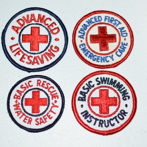 May include: Four round embroidered patches with red crosses and white backgrounds. The patches are for Advanced Lifesaving, Advanced First Aid Emergency Care, Basic Water Rescue Safety, and Basic Swimming Instructor.