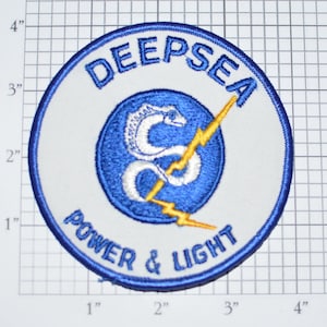 May include: Embroidered patch with the words "DEEPSEA POWER & LIGHT" in blue lettering. The patch features a blue and white design with a stylized "S" and a yellow lightning bolt. The patch measures approximately 4 inches in diameter.