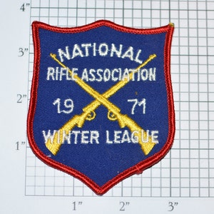 May include: A blue and red embroidered patch with the text "NATIONAL RIFLE ASSOCIATION 1971 WINTER LEAGUE" and two crossed rifles in gold thread.