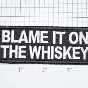 May include: Black rectangular patch with the embroidered text "BLAME IT ON THE WHISKEY" in white. The patch measures approximately 4 inches wide and 2 inches tall.