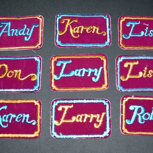 May include: Nine embroidered name patches with names like "Andy", "Karen", and "Lisa". Each patch has a burgundy background, a gold border, and the name in a contrasting color. The patches are rectangular.