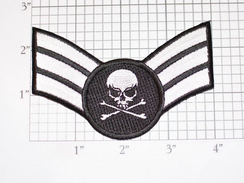 Op de afbeelding: Een zwart-wit geborduurde patch met een doodshoofd en gekruiste botten ontwerp. De patch heeft een cirkelvormig midden met de schedel en botten, en twee schuine vleugels met elk drie witte strepen. De patch is ongeveer 10 cm breed.