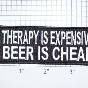 May include: Black embroidered patch with white text that reads "Therapy is expensive, beer is cheap".