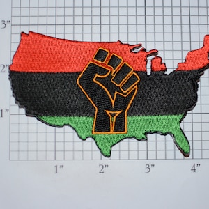 May include: Embroidered patch in the shape of the United States, featuring the Pan-African colors of red, black, and green. A black fist with an orange outline is centered on the patch. The patch measures approximately 3 inches wide.