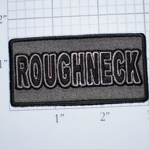 May include: A gray embroidered patch with the word "ROUGHNECK" in black with a white outline.