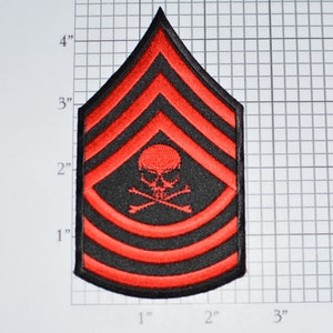 May include: Red and black embroidered patch with a skull and crossbones design. The patch has five red stripes and is shaped like a chevron. The patch is approximately 4 inches tall and 3 inches wide.
