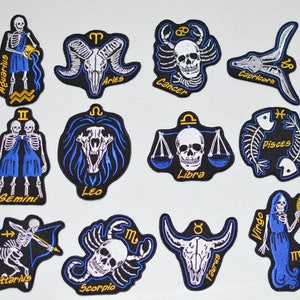 May include: Twelve embroidered iron-on patches featuring the astrological signs of the zodiac. Each patch is black with white and blue embroidery. The signs are: Aquarius, Aries, Cancer, Capricorn, Gemini, Leo, Libra, Pisces, Sagittarius, Scorpio, Taurus, and Virgo.