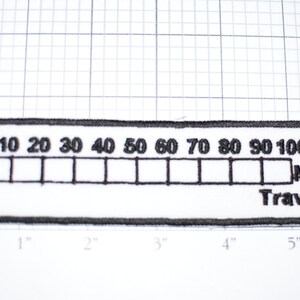 May include: Black and white embroidered patch with a mileage counter design. The counter reads "0 10 20 30 40 50 60 70 80 90 100,000 Miles Traveled".