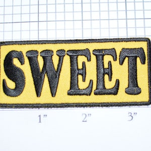 May include: A yellow embroidered patch with black stitching that reads "SWEET".