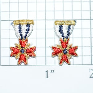 May include: Two red and gold embroidered patches with a white and blue ribbon. The patches feature a red cross with gold accents and a blue center.