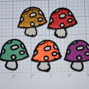 May include: Five embroidered iron-on patches of different colored mushrooms with white spots. The mushrooms are in shades of green, orange, red, purple, and gold.