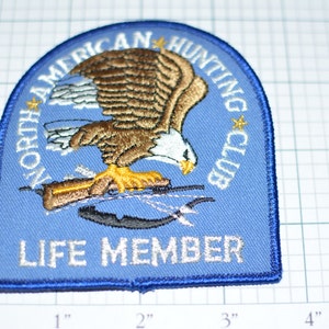 May include: Blue embroidered patch with a white eagle, a rifle, and the text "North American Hunting Club" and "Life Member".