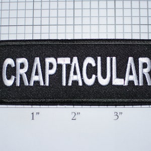 May include: A black fabric patch with white embroidered text that reads "CRAPTACULAR".