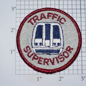 May include: A red, white, and blue embroidered patch with the text "TRAFFIC SUPERVISOR" in a white circle with a red border. The center of the circle features a stylized image of a traffic light.