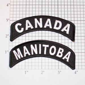 May include: Two black and white embroidered patches. The top patch says "CANADA" in white lettering on a black background. The bottom patch says "MANITOBA" in white lettering on a black background.