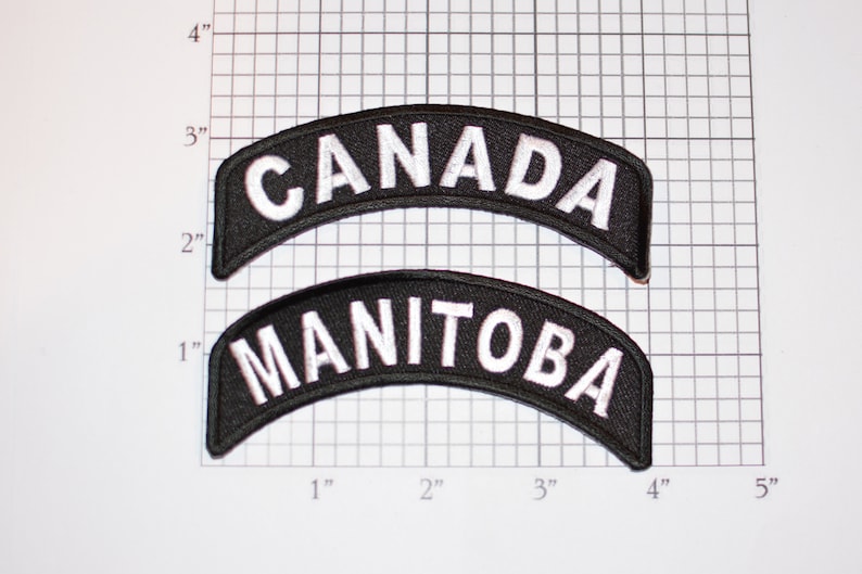 May include: Two black and white embroidered patches. The top patch says "CANADA" in white lettering on a black background. The bottom patch says "MANITOBA" in white lettering on a black background.