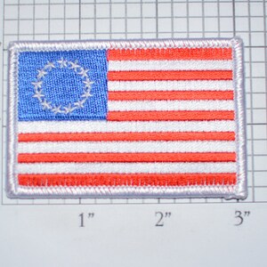 May include: A 2-inch by 3-inch embroidered patch of the first American flag with 13 stars in a circle on a blue field and 13 red and white stripes.