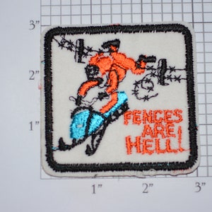 May include: An embroidered patch with a cartoon image of a person on a snowmobile crashing into a barbed wire fence. The text "FENCES ARE HELL" is written in orange thread below the image.