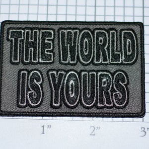 May include: A black and gray embroidered patch with the text "The World Is Yours".