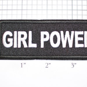 May include: Black embroidered patch with white text that reads "GIRL POWER".