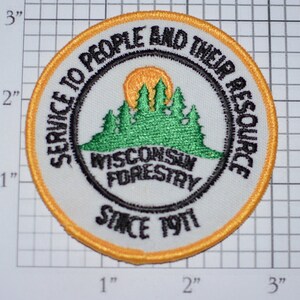 May include: A white embroidered patch with a yellow border. The patch features a green forest scene with a sun, the text "SERVICE TO PEOPLE AND THEIR RESOURCE", "WISCONSIN FORESTRY", and "SINCE 1911".