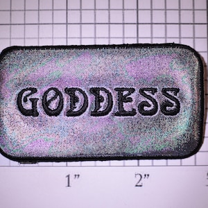 May include: A silver iridescent fabric patch with black embroidered text that reads "GODDESS". The patch is approximately 2 inches wide and 1 inch tall.