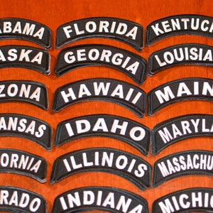 Puede incluir: Un conjunto de parches bordados negros en forma de arco, cada uno con el nombre de un estado estadounidense en letras blancas. Incluyen: Pennsylvania, Rhode Island, South Carolina, South Dakota, Tennessee y Texas.
