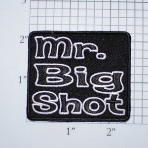 May include: Black embroidered patch with white lettering that reads "Mr. Big Shot" on a black background.