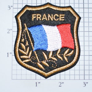 May include: A black embroidered patch with a gold border, featuring the French flag and the word "FRANCE". The patch is approximately 2 inches wide and 3 inches tall.