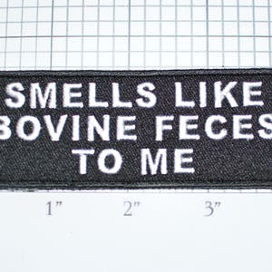 May include: Black embroidered patch with white text that reads "Smells like bovine feces to me".