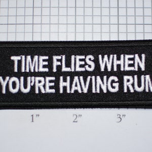 May include: Black embroidered patch with white text that reads "TIME FLIES WHEN YOU'RE HAVING RUM".