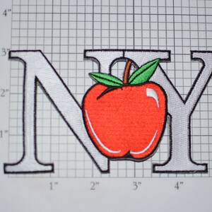 May include: White embroidered patch with the letters "NY" in a large font. A red apple with a green stem and leaves is centered between the letters.