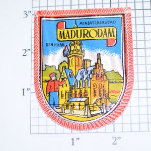 May include: A red, white, and blue embroidered patch with the text "MINIATUURSTAD MADURODAM DEN HAAG" and a depiction of a miniature city with a tall tower.