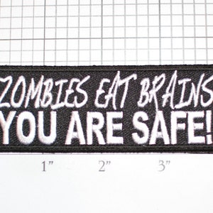 May include: Black embroidered patch with white text that reads "Zombies Eat Brains You Are Safe!"