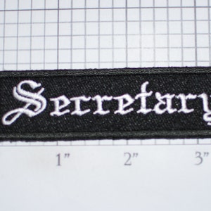 May include: Black fabric patch with white embroidered text that reads "Secretary" in a gothic font.