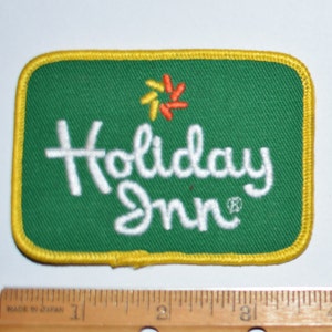 May include: A green and yellow embroidered patch with the words "Holiday Inn" in white lettering and a stylized star in orange and yellow.