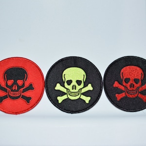 May include: Three embroidered skull and crossbones patches. One patch is red with a black skull, one is black with a green skull, and one is black with a red skull.