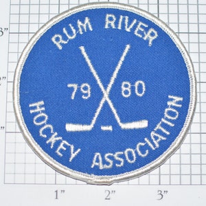 May include: A blue and white embroidered patch with the text "Rum River Hockey Association" and the years "79 80" around a pair of crossed hockey sticks.