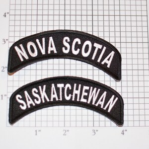 May include: Two black embroidered patches with white lettering. The top patch reads "NOVA SCOTIA" and the bottom patch reads "SASKATCHEWAN".