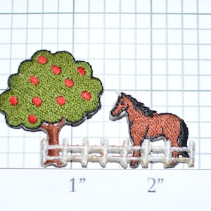 May include: An embroidered iron-on patch featuring a brown horse standing behind a white picket fence with a green tree with red apples in the background.